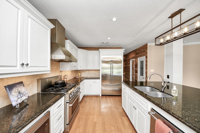 1140 Bartlett Rd, Katy, TX 77493 - kitchen with premium appliances, a sink, wall chimney exhaust hood, white cabinetry, and light wood-style floors