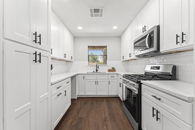 13430 Orleans St, Houston, TX 77015 - kitchen featuring stainless steel appliances, a sink, dark wood finished floors, white cabinets, and recessed lighting