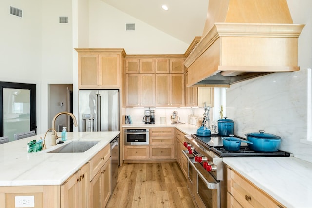 2176 Hwy 87, Gilchrist, TX 77617 - kitchen featuring appliances with stainless steel finishes, light brown cabinetry, custom range hood, high vaulted ceiling, and a sink