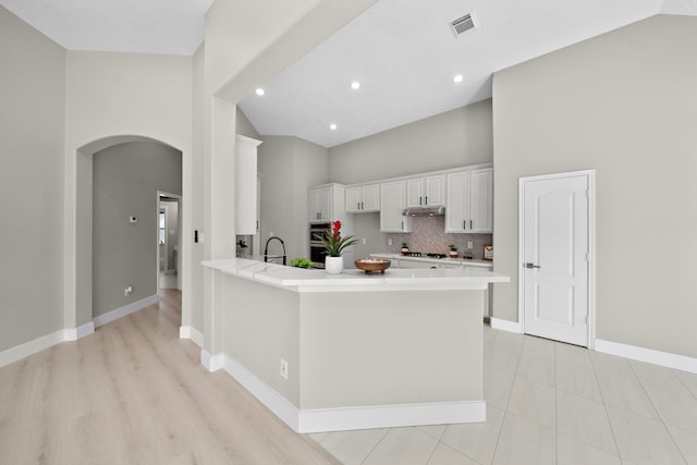 kitchen featuring arched walkways, high vaulted ceiling, a peninsula, under cabinet range hood, and white cabinets