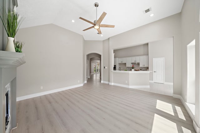 unfurnished living room featuring arched walkways, a ceiling fan, light wood-style floors, a high end fireplace, and recessed lighting