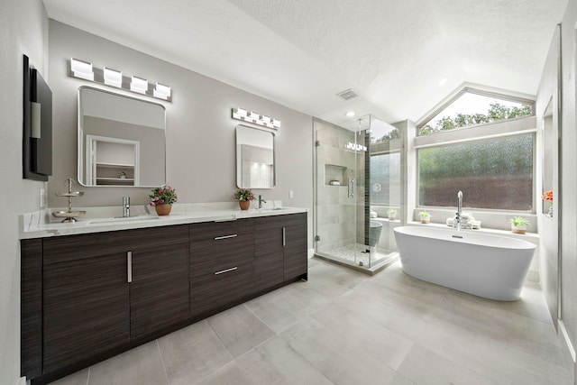 bathroom with a stall shower, double vanity, vaulted ceiling, a freestanding bath, and a textured ceiling