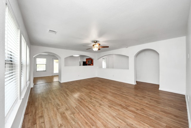 5818 Taylan Ln, Rosenberg, TX 77471 - unfurnished living room featuring a ceiling fan, light wood-type flooring, arched walkways, and baseboards