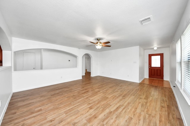 5818 Taylan Ln, Rosenberg, TX 77471 - unfurnished living room with light wood finished floors, ceiling fan, arched walkways, baseboards, and a textured ceiling