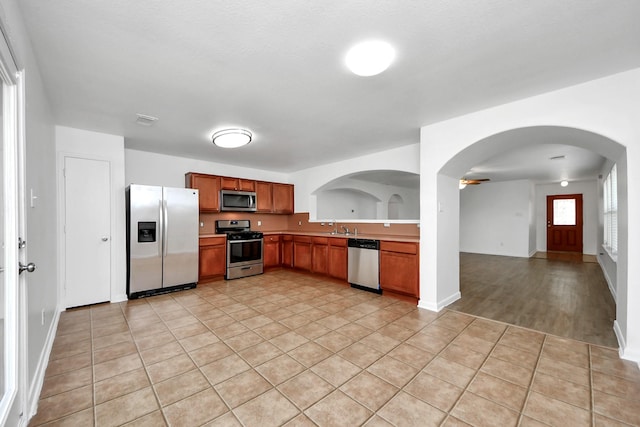 5818 Taylan Ln, Rosenberg, TX 77471 - kitchen featuring appliances with stainless steel finishes, arched walkways, brown cabinetry, a sink, and light countertops