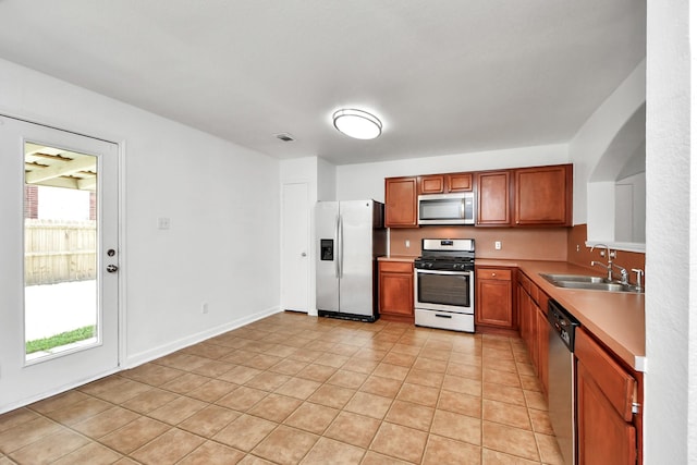 5818 Taylan Ln, Rosenberg, TX 77471 - kitchen featuring appliances with stainless steel finishes, a sink, light countertops, light tile patterned flooring, and brown cabinetry