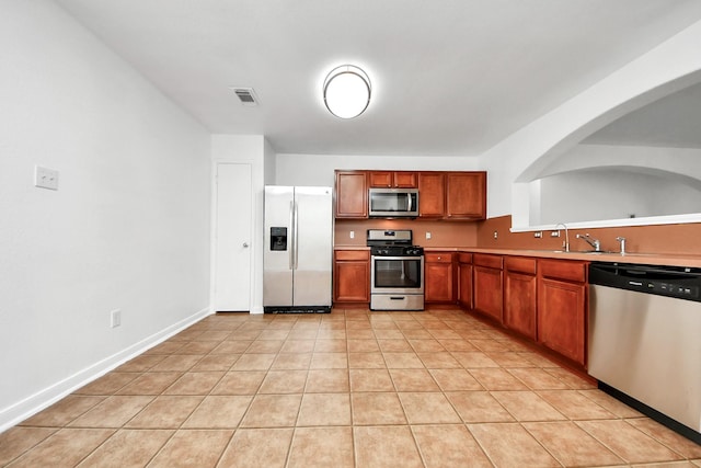 5818 Taylan Ln, Rosenberg, TX 77471 - kitchen featuring appliances with stainless steel finishes, light tile patterned floors, brown cabinets, light countertops, and arched walkways