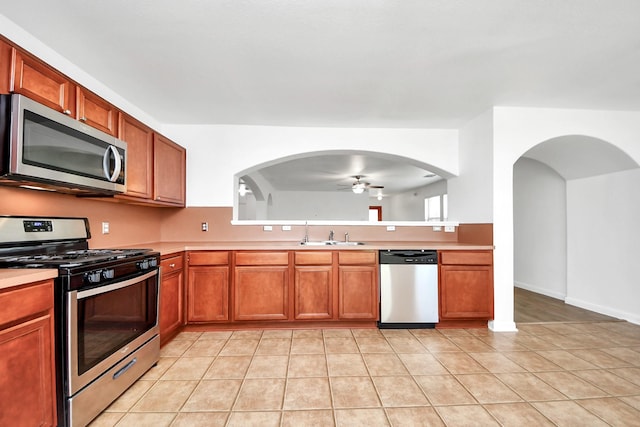 5818 Taylan Ln, Rosenberg, TX 77471 - kitchen with appliances with stainless steel finishes, ceiling fan, arched walkways, light countertops, and brown cabinets