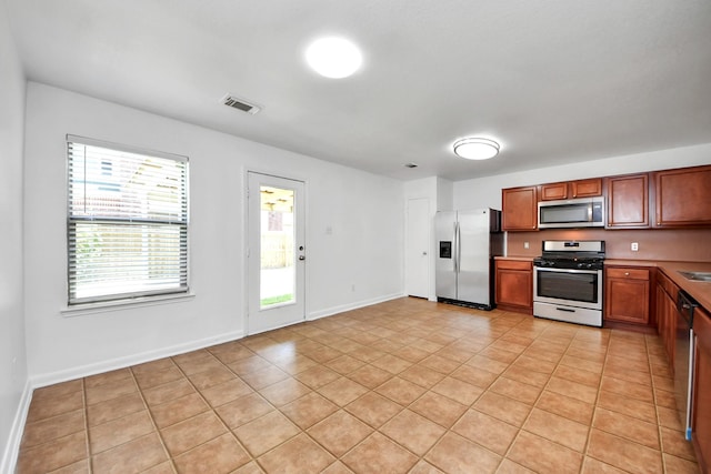 5818 Taylan Ln, Rosenberg, TX 77471 - kitchen with stainless steel appliances, light tile patterned flooring, brown cabinets, and baseboards