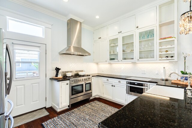 1717 Winnie St, Galveston, TX 77550 - kitchen featuring wall chimney range hood, appliances with stainless steel finishes, white cabinetry, dark wood-style flooring, and dark stone counters