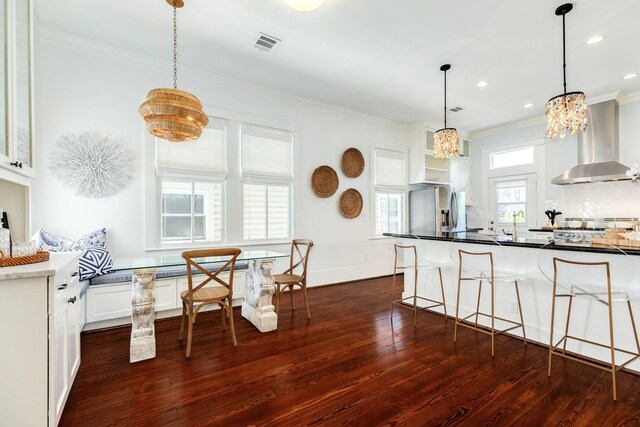 1717 Winnie St, Galveston, TX 77550 - kitchen with wall chimney range hood, dark wood-style flooring, ornamental molding, a chandelier, and a breakfast bar area