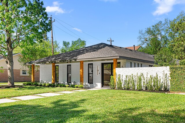 view of front of property featuring brick siding, a front yard, covered porch, and roof with shingles