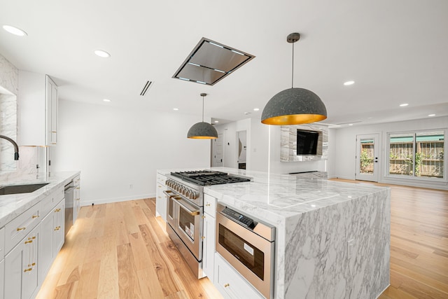 kitchen with appliances with stainless steel finishes, a sink, open floor plan, white cabinets, and light wood-style floors