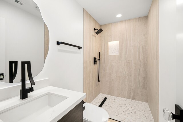 bathroom with toilet, a tile shower, vanity, and recessed lighting