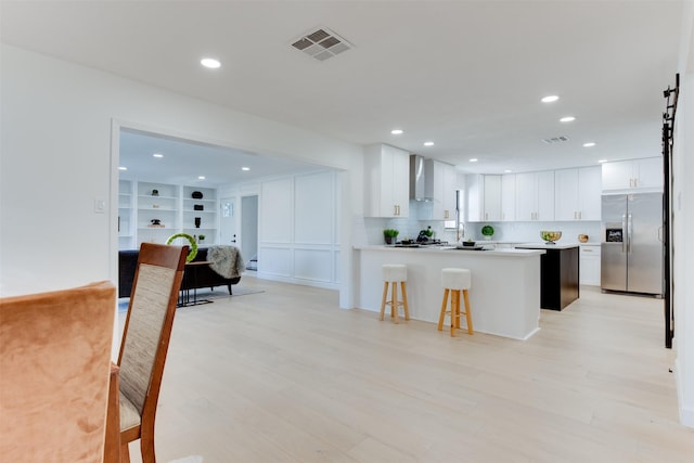 2514 Haverhill Dr, Houston, TX 77008 - kitchen with stainless steel refrigerator with ice dispenser, wall chimney range hood, a breakfast bar, light countertops, and light wood-style floors