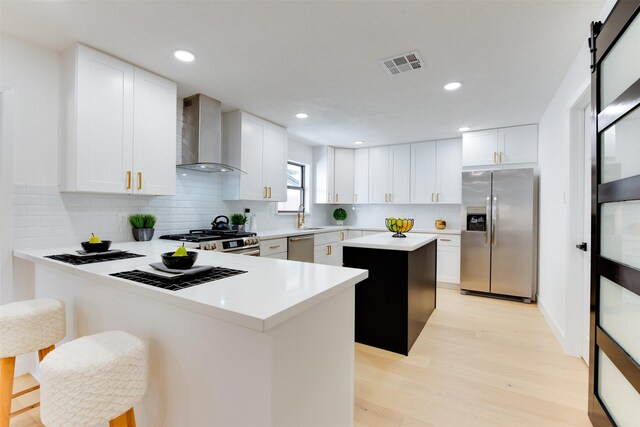 2514 Haverhill Dr, Houston, TX 77008 - kitchen featuring appliances with stainless steel finishes, wall chimney range hood, light wood finished floors, a center island, and a sink
