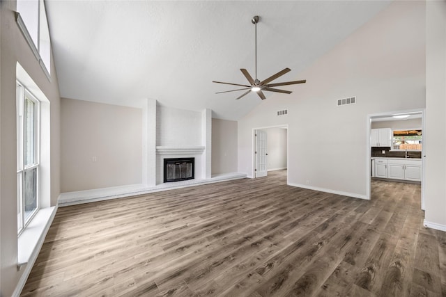 unfurnished living room featuring ceiling fan, high vaulted ceiling, wood finished floors, a large fireplace, and a sink