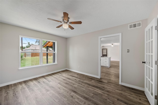 unfurnished room with a ceiling fan, wood finished floors, baseboards, french doors, and a textured ceiling