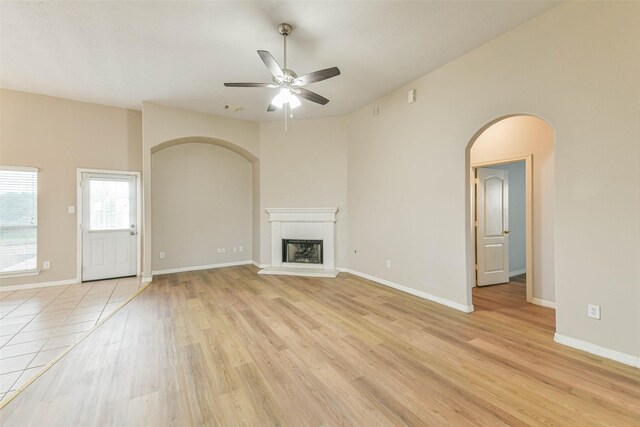 2212 Highland Crossing Dr, Conroe, TX 77304 - unfurnished living room with a ceiling fan, arched walkways, light wood-style floors, a fireplace with raised hearth, and baseboards