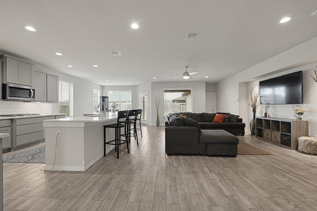 living room with light wood-type flooring, recessed lighting, a ceiling fan, and baseboards