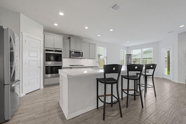 kitchen featuring stainless steel appliances, a sink, light wood finished floors, a center island with sink, and recessed lighting