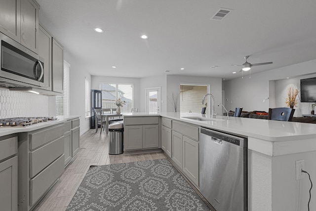 kitchen featuring appliances with stainless steel finishes, a sink, gray cabinetry, light countertops, and recessed lighting