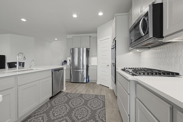 kitchen with stainless steel appliances, a sink, tasteful backsplash, light countertops, and recessed lighting