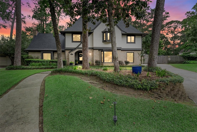 english style home featuring stucco siding, brick siding, and a shingled roof