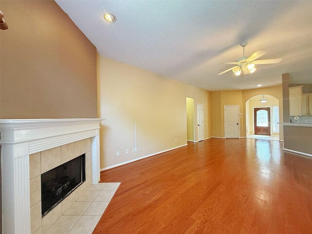 16322 E Amber Willow Trl, Cypress, TX 77433 - unfurnished living room featuring a fireplace, a ceiling fan, arched walkways, light wood-style floors, and baseboards