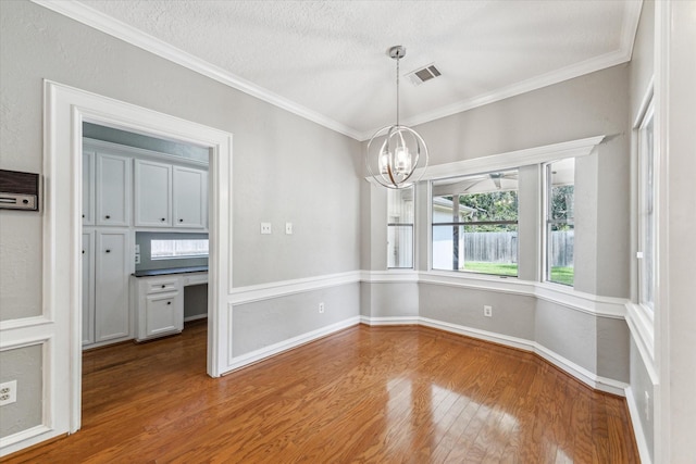 unfurnished dining area with a chandelier, wood finished floors, ornamental molding, baseboards, and a textured ceiling