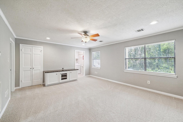 unfurnished room featuring crown molding, a ceiling fan, baseboards, light carpet, and washer / clothes dryer