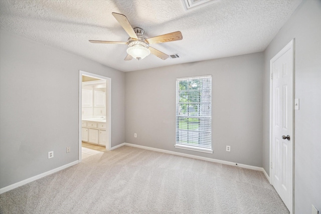 unfurnished bedroom featuring light carpet, baseboards, a textured ceiling, ensuite bath, and a ceiling fan