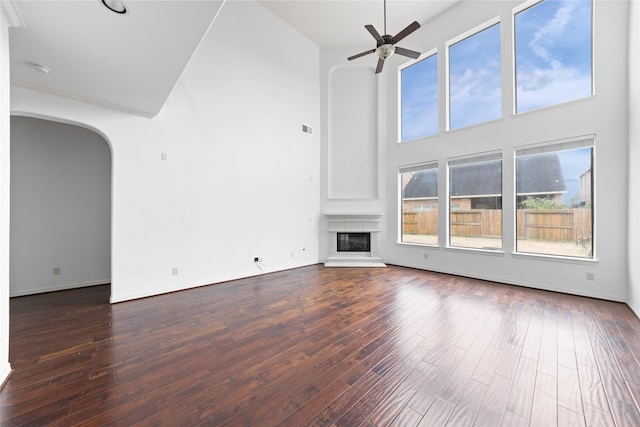 17803 Paint Bluff Ln, Cypress, TX 77433 - unfurnished living room featuring arched walkways, a towering ceiling, a ceiling fan, dark wood finished floors, and a glass covered fireplace