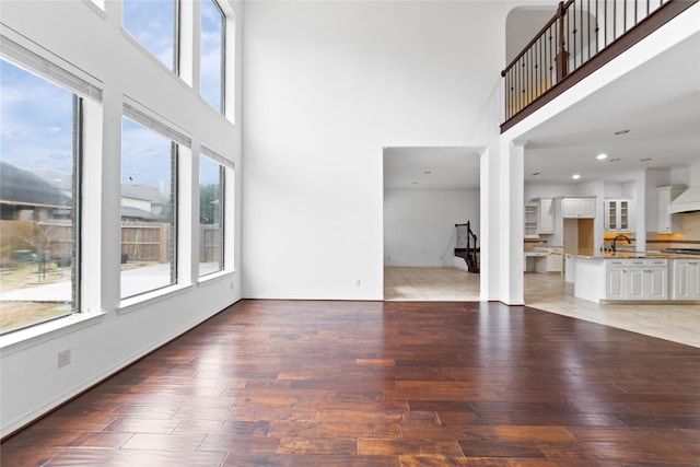 17803 Paint Bluff Ln, Cypress, TX 77433 - unfurnished living room with a towering ceiling, light wood-style flooring, baseboards, and a sink
