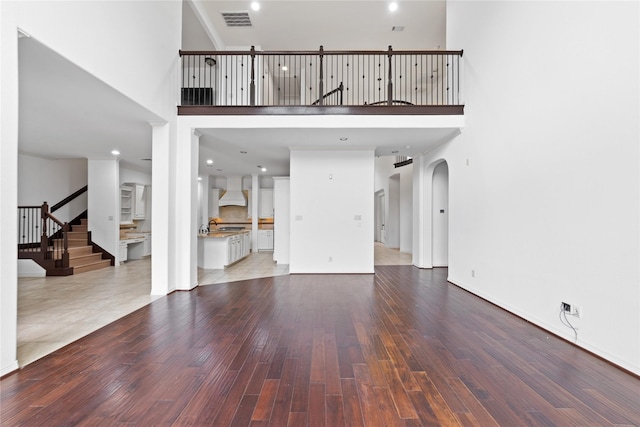 17803 Paint Bluff Ln, Cypress, TX 77433 - unfurnished living room featuring a towering ceiling, wood finished floors, arched walkways, stairway, and recessed lighting