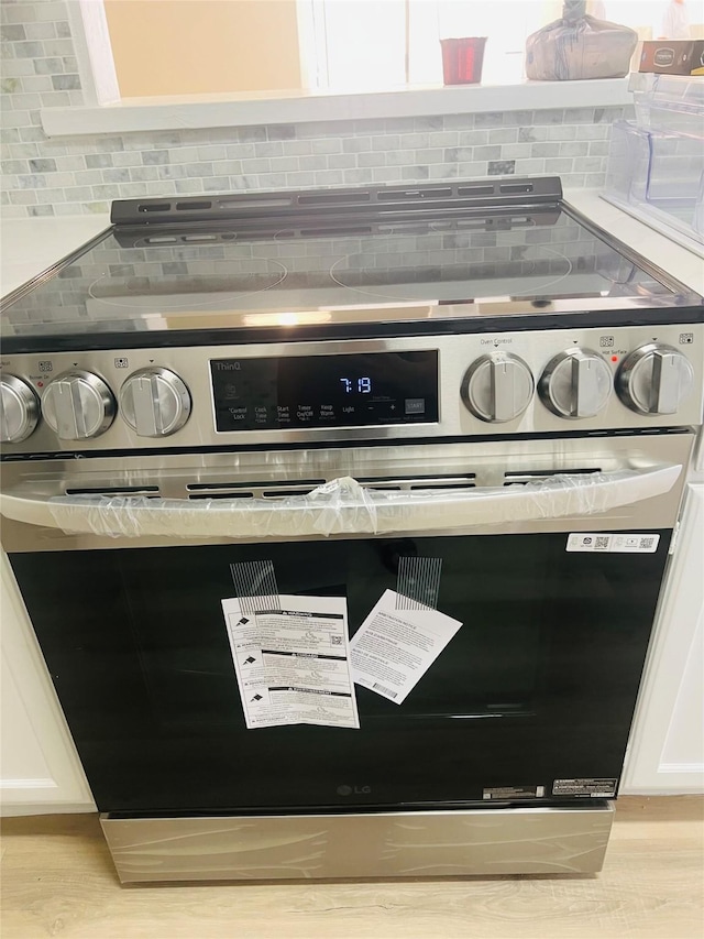 2668 Bering Dr Unit 2668, Houston, TX 77057 - detailed view of stainless steel range with electric cooktop, backsplash, light wood finished floors, and white cabinets
