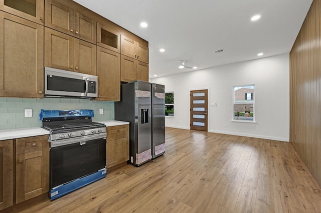 5731 Belvedere St, Houston, TX 77021 - kitchen with stainless steel appliances, light countertops, backsplash, light wood-style floors, and glass insert cabinets