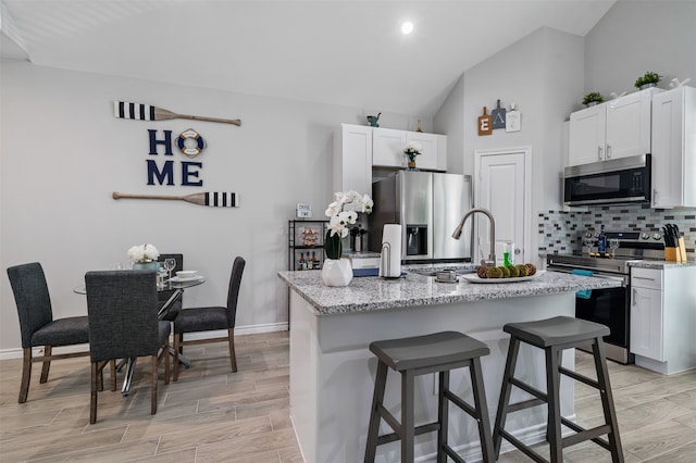 16858 W Alderson, Montgomery, TX 77316 - kitchen with appliances with stainless steel finishes, vaulted ceiling, decorative backsplash, a kitchen bar, and a center island with sink