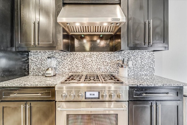 kitchen with high end stainless steel range oven, wall chimney exhaust hood, tasteful backsplash, and light stone counters