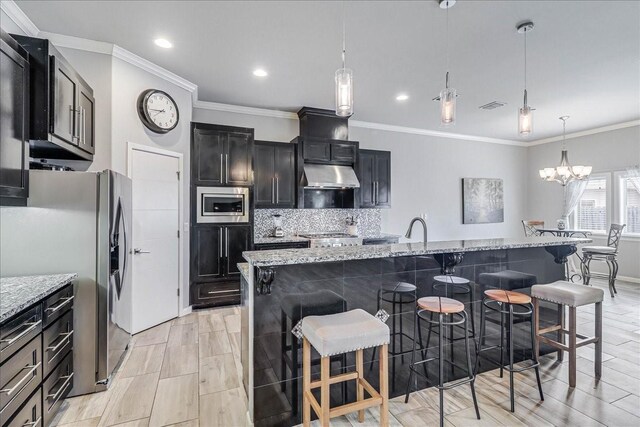 kitchen featuring appliances with stainless steel finishes, under cabinet range hood, a chandelier, tasteful backsplash, and a breakfast bar