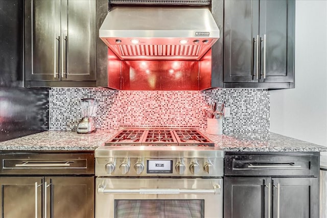kitchen featuring stainless steel gas range oven, wall chimney range hood, tasteful backsplash, and light stone counters