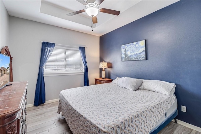 bedroom with wood finished floors, baseboards, a tray ceiling, and a ceiling fan