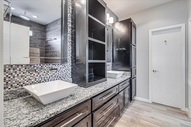 bathroom featuring wood finished floors, tasteful backsplash, double vanity, baseboards, and recessed lighting