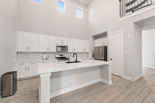 7010 Grassland Vista Ln, Katy, TX 77493 - kitchen with stainless steel appliances, a towering ceiling, light wood-type flooring, white cabinetry, and backsplash