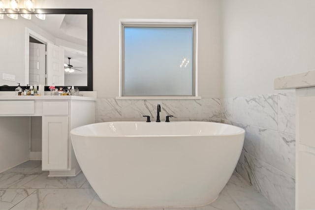 7010 Grassland Vista Ln, Katy, TX 77493 - bathroom featuring marble look tile flooring, a freestanding tub, vanity, tile walls, and wainscoting