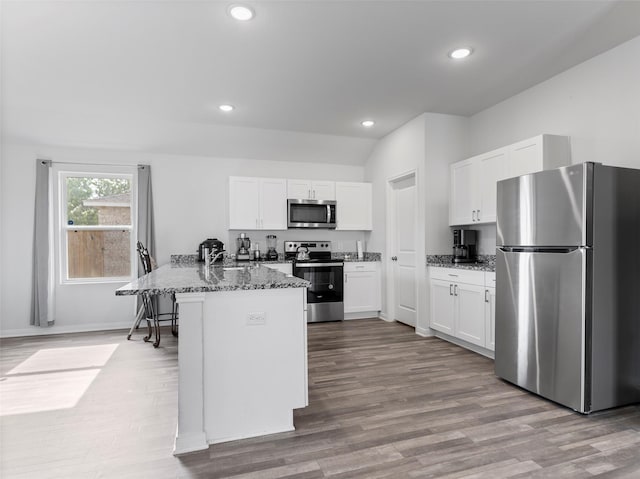 2715 Marguerite St, Bay City, TX 77414 - kitchen featuring stainless steel appliances, a peninsula, white cabinetry, wood finished floors, and dark stone countertops