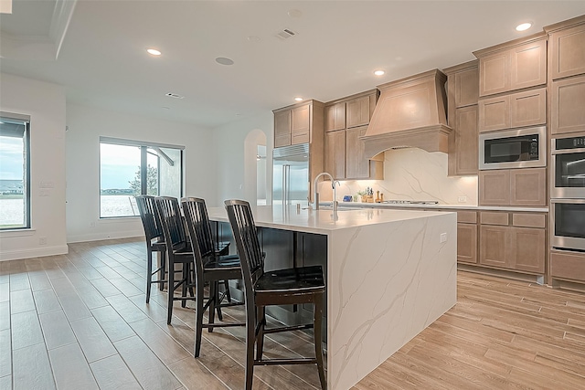 10615 Painted Crescent Ct, Cypress, TX 77433 - kitchen with built in appliances, custom range hood, a sink, light wood-type flooring, and a kitchen island with sink