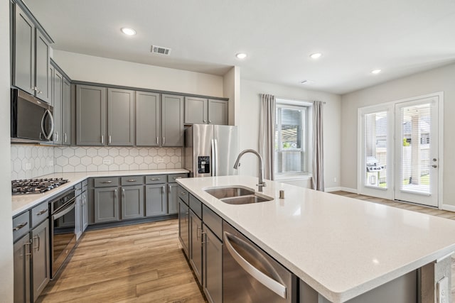10292 Bayou Oaks Dr, Conroe, TX 77385 - kitchen featuring stainless steel appliances, a sink, light wood-style flooring, gray cabinets, and decorative backsplash