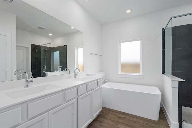 bathroom featuring a stall shower, double vanity, wood finished floors, a freestanding tub, and recessed lighting