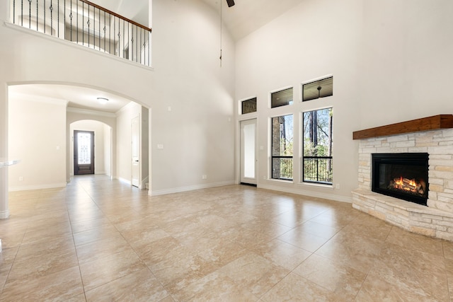 32 Evangeline Blvd, Conroe, TX 77304 - unfurnished living room with a stone fireplace, ceiling fan, baseboards, a towering ceiling, and arched walkways